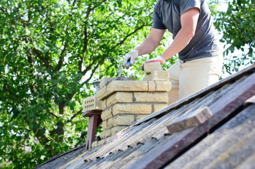 A bricklayer repairing a brick chimney on the rooftop of a house with an asbestos roof. The worker is wearing protective gear while carefully replacing or fixing damaged bricks and mortar to restore the chimney’s structure. The asbestos roofing panels and surrounding roof area are visible, emphasizing safe construction practices and professional masonry work at height.