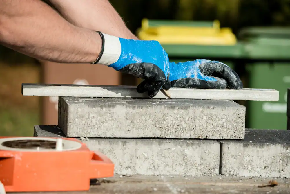 A professional mason performing masonry work in Middlesex County, Massachusetts. The worker is carefully laying bricks and applying mortar, wearing protective gloves and work gear. Construction tools, such as trowels, buckets of mortar, and scaffolding, are visible around the worksite. The image captures the hands-on process of building or repairing a brick structure, highlighting skilled craftsmanship in residential or commercial masonry construction.