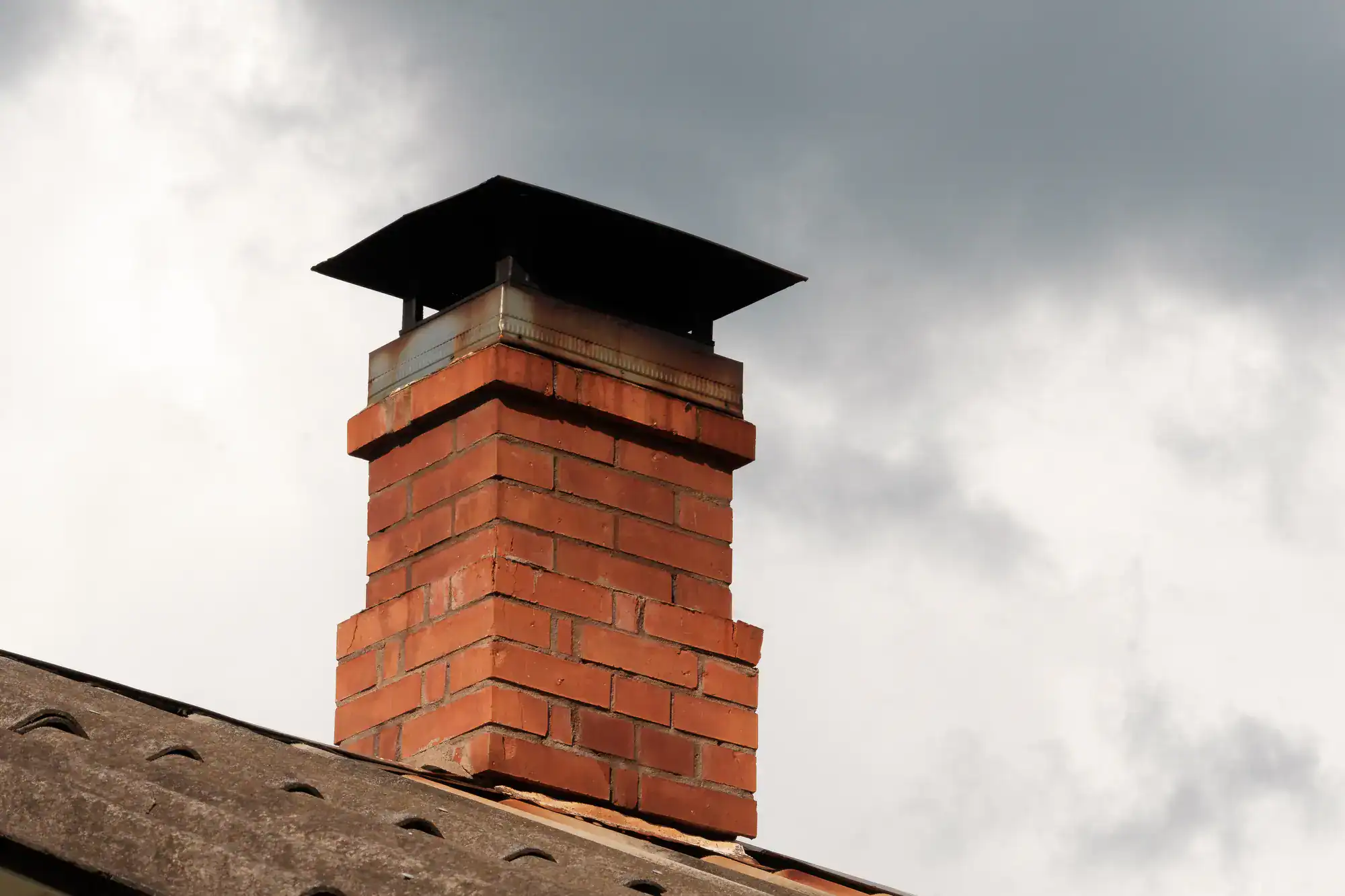 Red brick chimney standing tall against a cloudy gray sky, showcasing detailed masonry work for Academy Masonry.