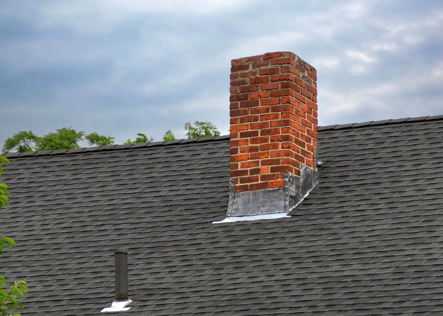 Brick chimney atop a residential rooftop against a clear blue sky, showcasing masonry craftsmanship and clean brickwork for Academy Masonry.
