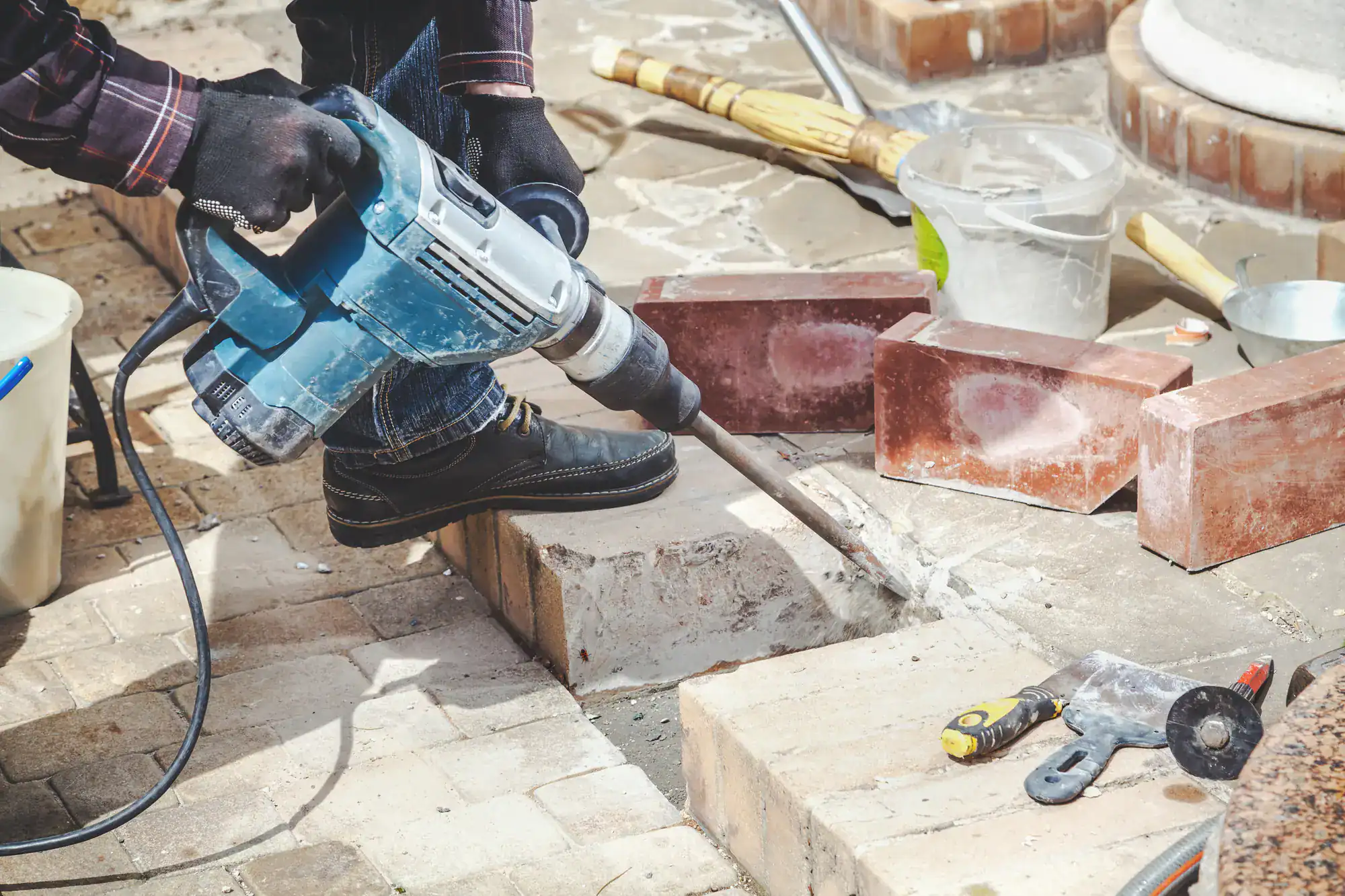 Construction worker wearing a hard hat and safety vest using a jackhammer on a concrete surface at a job site, representing Academy Masonry’s professional masonry services
