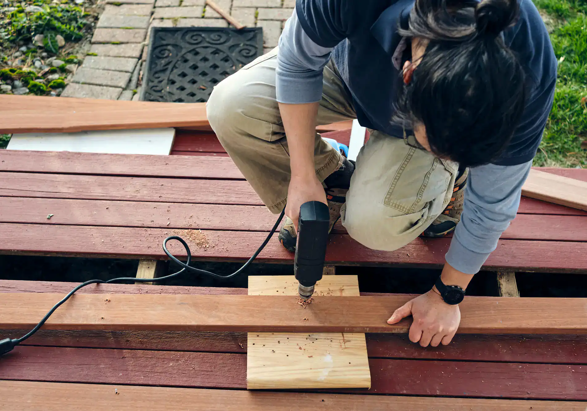 Construction worker using a drill on a wooden deck, installing or securing boards, demonstrating professional craftsmanship for Academy Masonry.