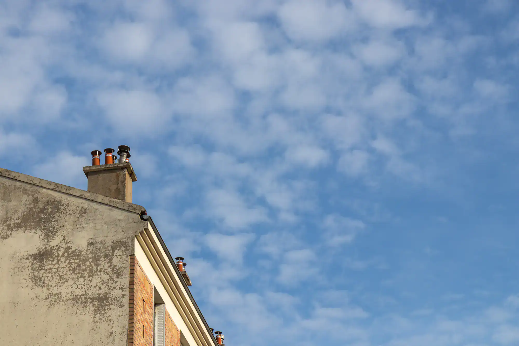 Rooftop chimney rising above a residential roof under a cloudy, overcast sky, symbolizing expert masonry work by Academy Masonry.