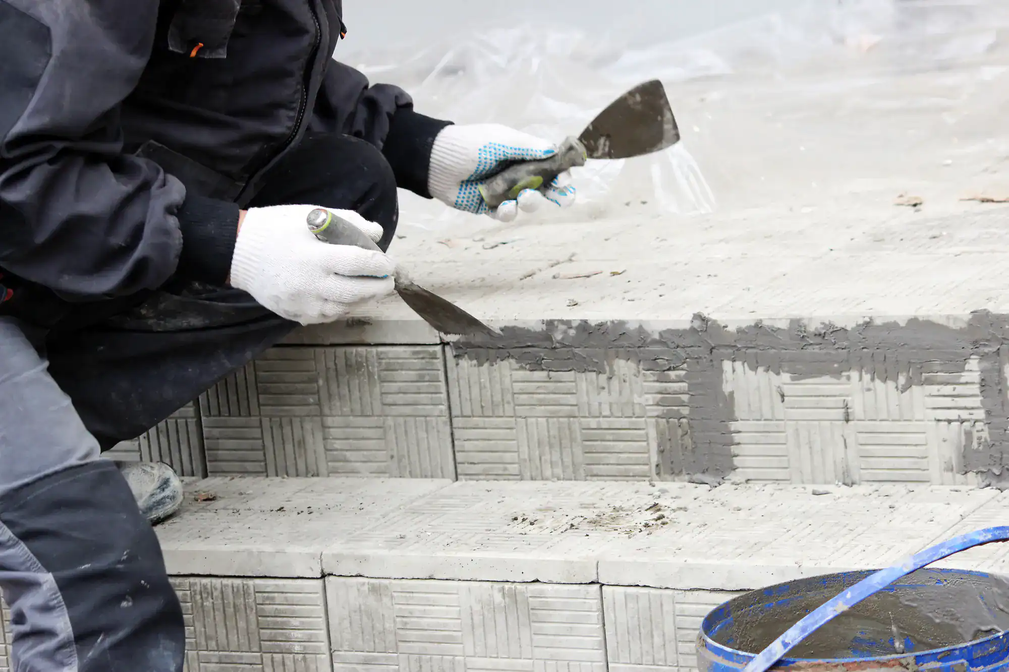 Skilled mason from Academy Masonry carefully installing ceramic tiles on outdoor stairs, using precision tools and adhesive for a clean, professional finish during a stair construction project